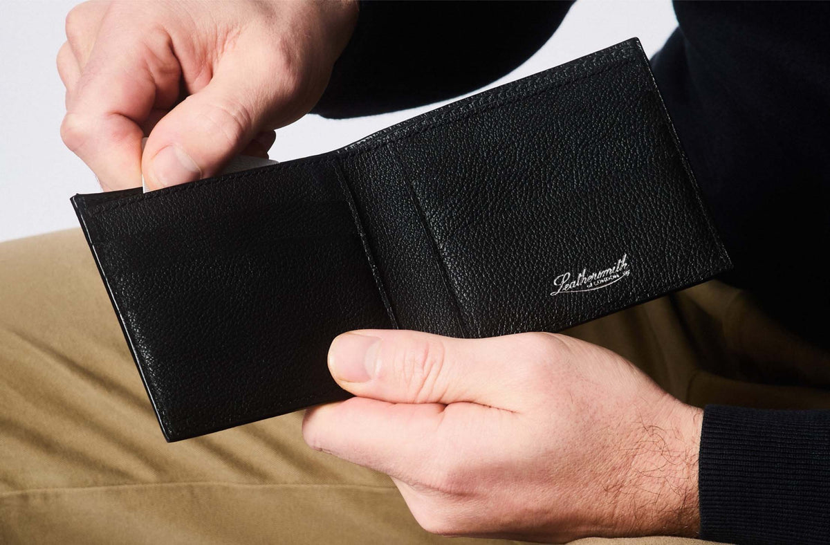 Black leather wallet with Leathersmith of London logo held open in hands